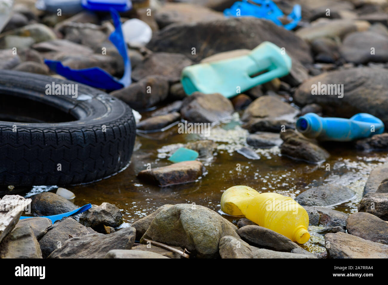 Les bouteilles en plastique et de pneu de voiture dans la boue de l'eau huileuse stream Banque D'Images