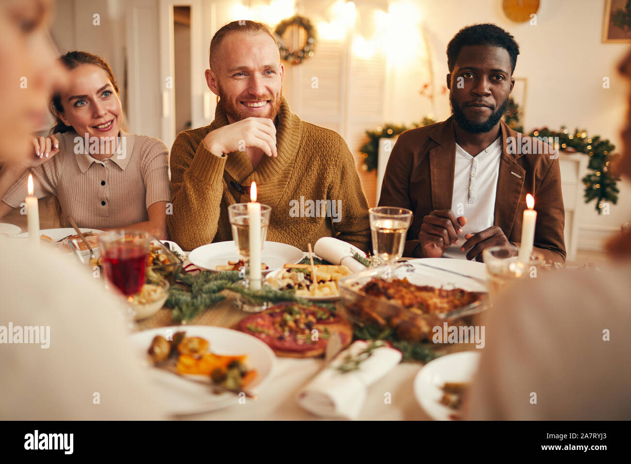 Poirtrait de groupe multi-ethnique de personnes appréciant le dîner assis à table avec de la nourriture délicieuse, l'accent sur l'homme barbu souriant dans le centre Banque D'Images