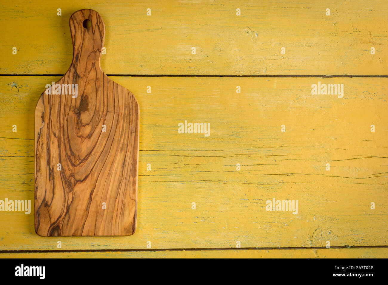 Planche à découper en bois d'olivier sur fond jaune avec copie espace rustique. Mise à plat. Banque D'Images
