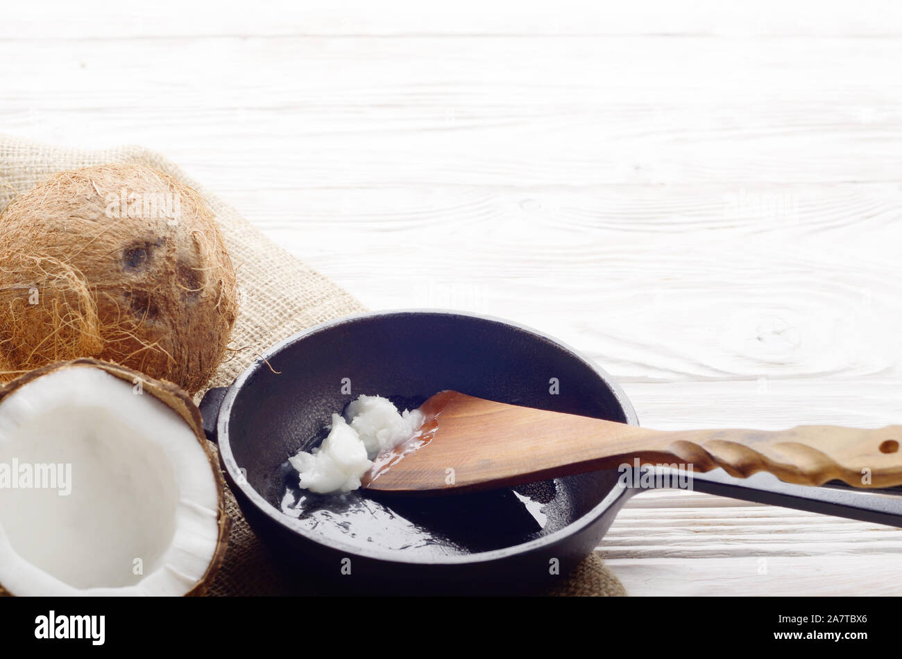 Coquille de noix de coco, avec de la viande, poêle en fonte et la spatule sur le chanvre sacs sur une table de cuisine en bois blanc Banque D'Images