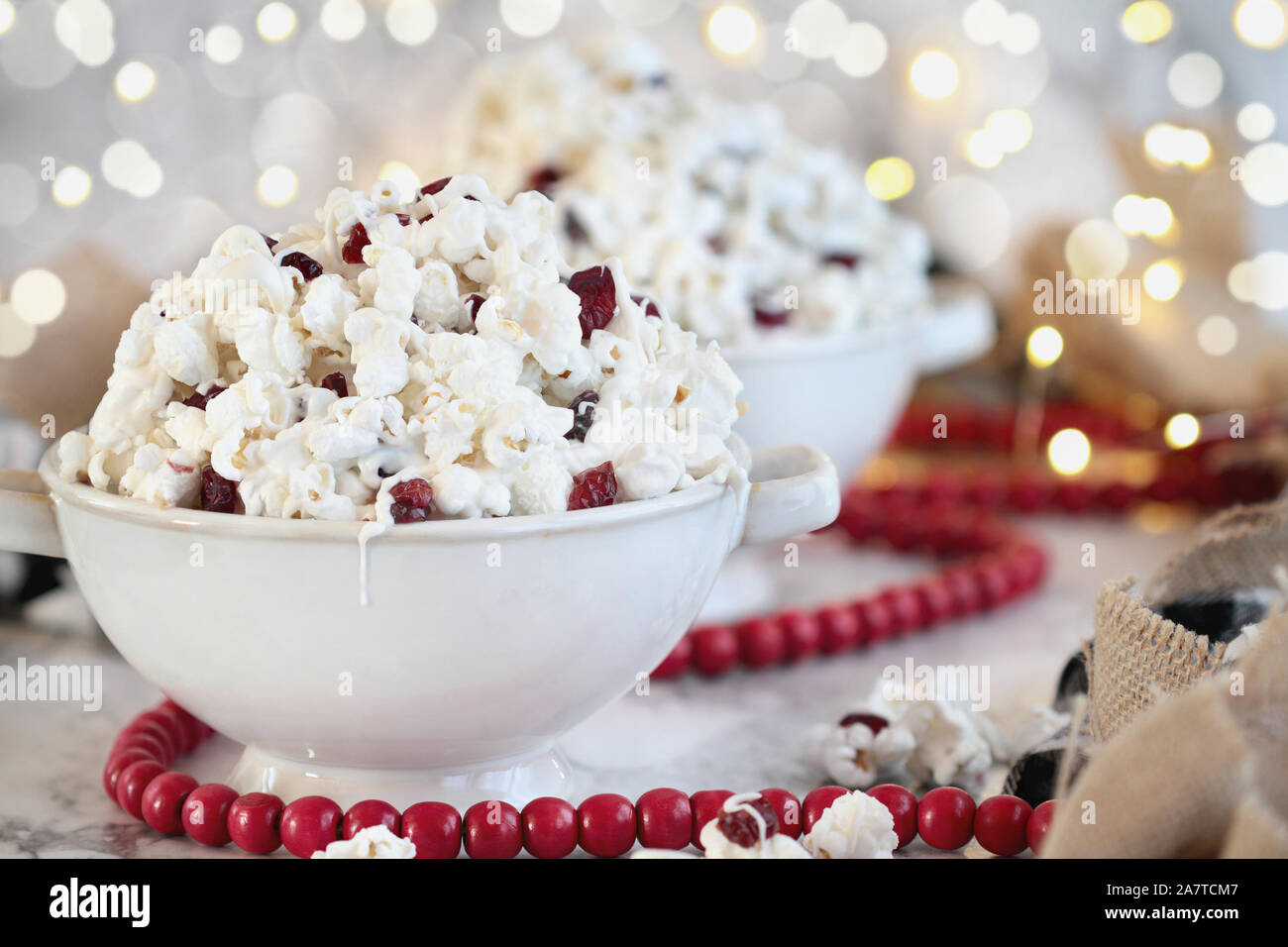 Bols de pop-corn et des canneberges séchées et snack-couverts dans le chocolat blanc prêt pour les vacances, entouré de lumières et de flou perle rouge garland. Banque D'Images