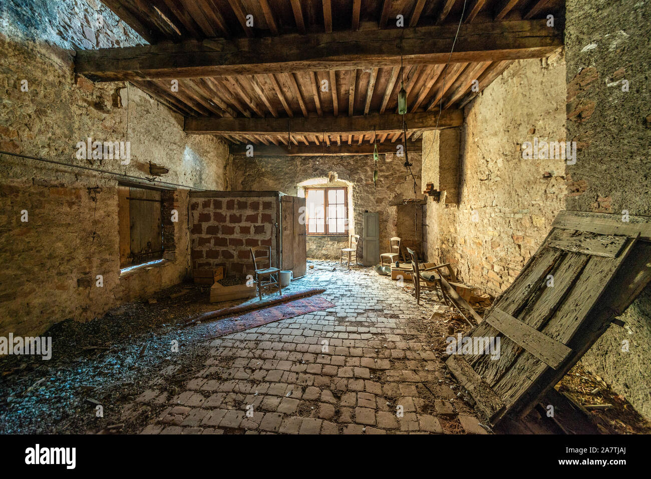 Une chambre abandonnée recouverte de poussière dans une maison médiévale française, avec poutres en bois intactes et carrelage au sol, illuminée par la lumière naturelle de la fenêtre. Banque D'Images