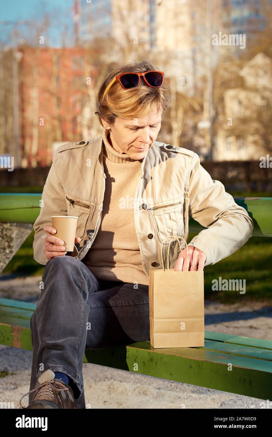 Les sièges d'une femme sur le banc dans un parc, profiter de la pause déjeuner. Papier, eco tasse et sac. Banque D'Images