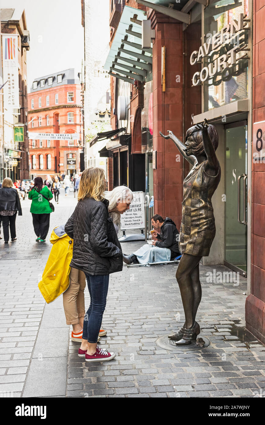 Les touristes inspecter une Cilla Black statue dans la caverne du quart de Liverpool, UK avec un mendiant dans l'arrière-plan. Banque D'Images