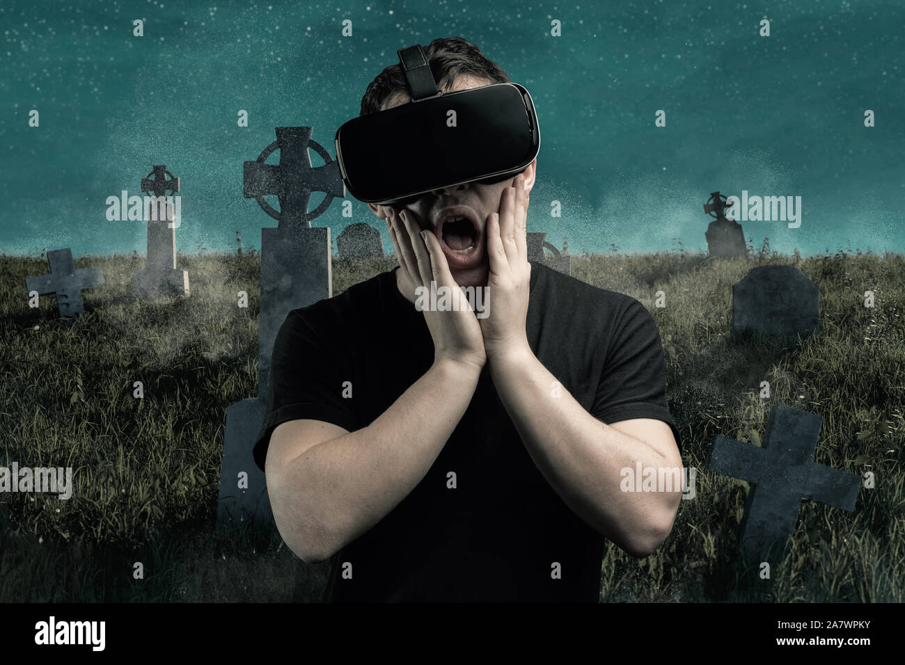 Jeune homme effrayant avec de l'expérience dispositif vr jouer jeu d'horreur en face de spooky graveyard Banque D'Images