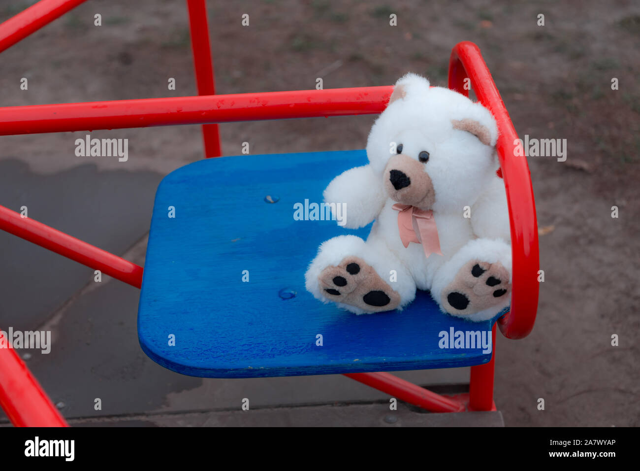 Close-up un ours est assis sur une balançoire pour les enfants en rouge. La notion de tristesse, la perte, la mort, le deuil, l'orphelin ou la solitude Banque D'Images