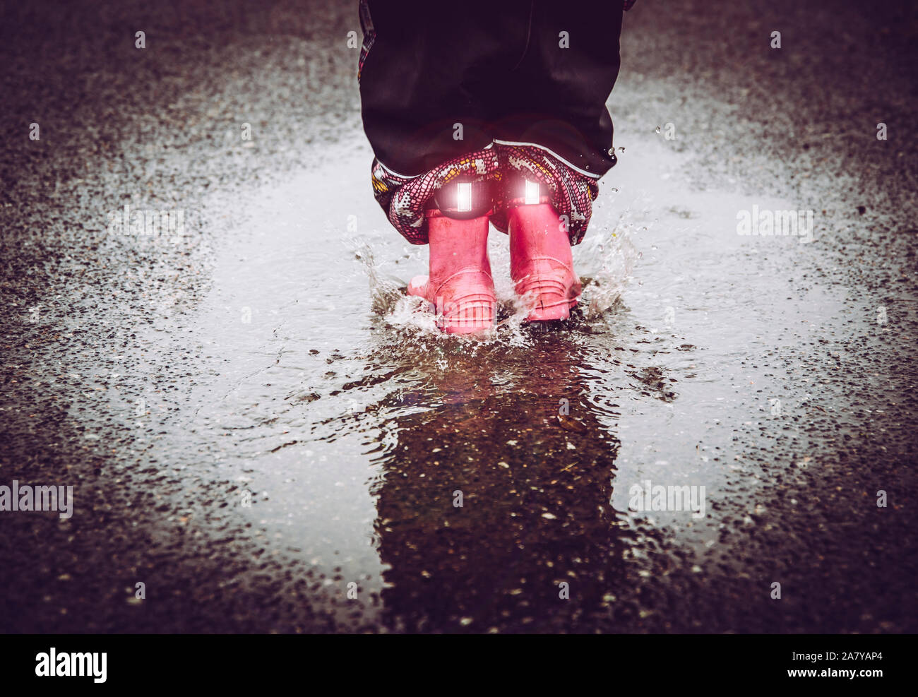 Girl having fun, sauter dans l'eau flaque sur la rue mouillée, portant des bottes de pluie Avec détails réfléchants rayures tissu brillant. Une grande visibilité et sécurité i Banque D'Images