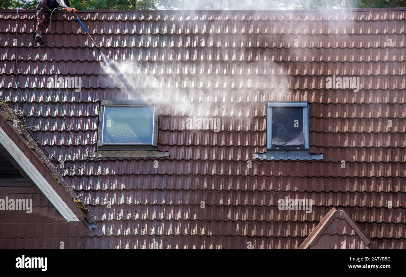 Homme travaillant laver des bardeaux de toit en pierre inclinés avec un nettoyeur sous pression d'eau pour enlever la saleté, la mousse et le lichen à l'extérieur en été. Service de nettoyage du toit Banque D'Images