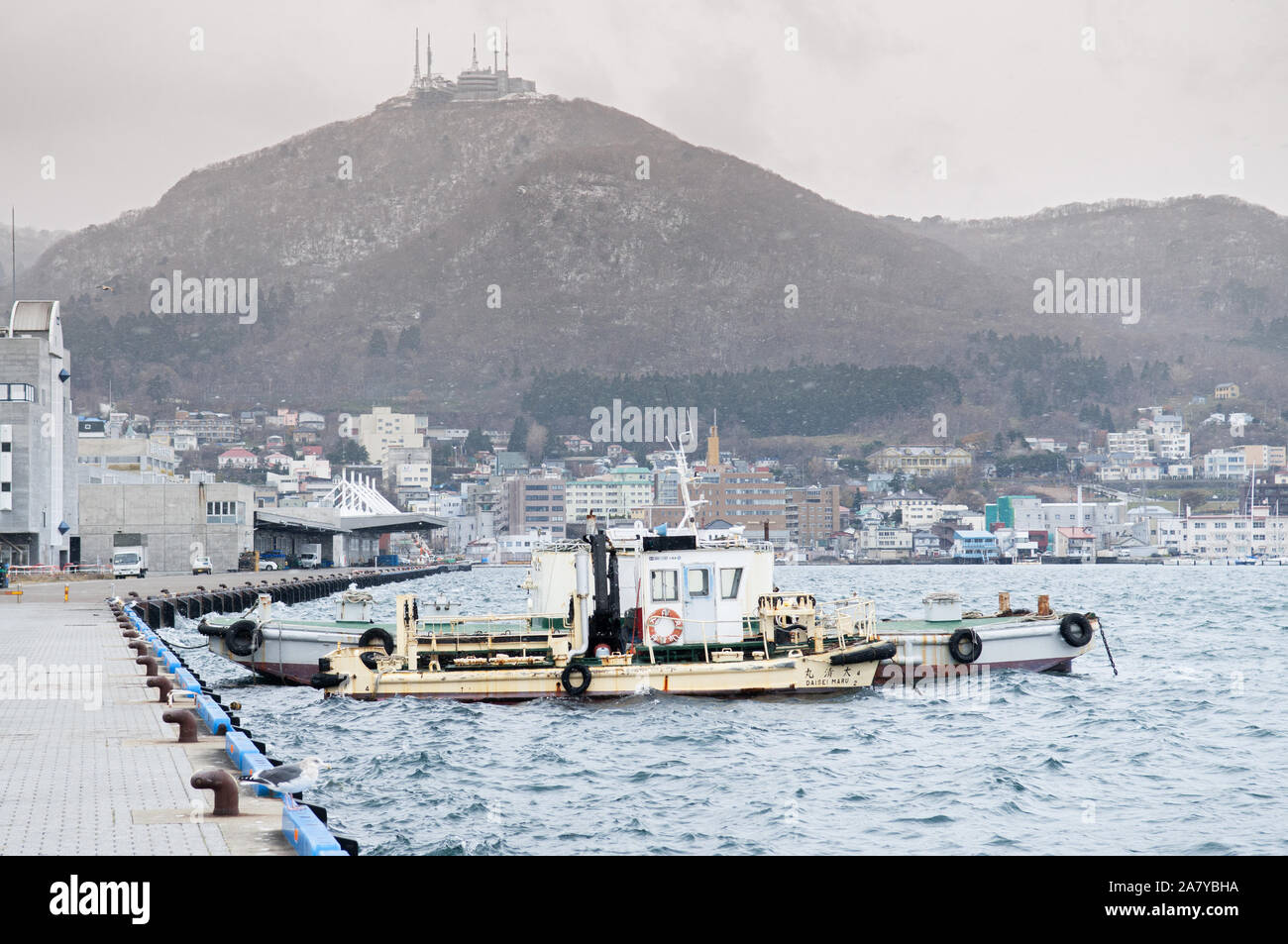 1 DÉC 2018 Hakkodate, Japon - Hakkodate Toyokawa pier port avec bateaux de pêche d'hiver dans l'atmosphère brumeuse et mont Hakkodate en arrière-plan. Banque D'Images