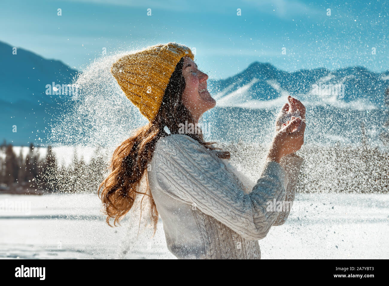 Happy girl joue avec poudre de neige contre forêt et montagnes Banque D'Images