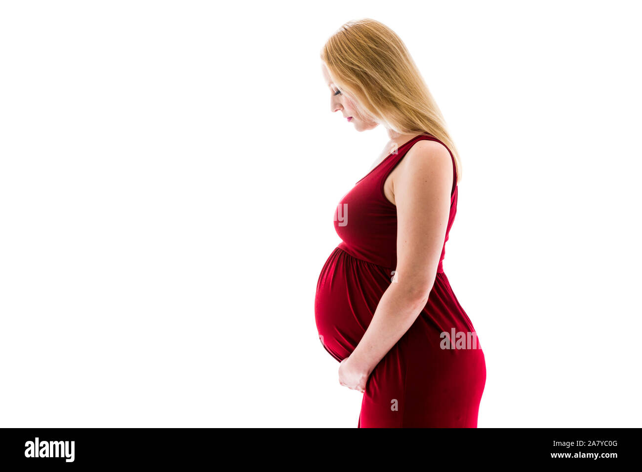Femme enceinte en robe rouge holding belly sur fond blanc. Portrait d'excité, heureux, blonde, jeune femme enceinte en studio photo. Concept de mat Banque D'Images