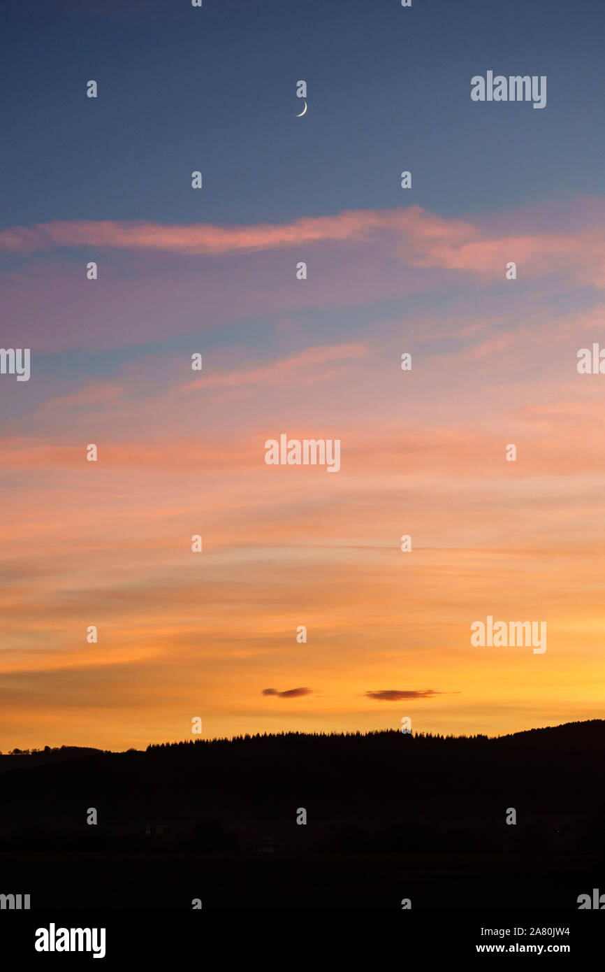 Une nouvelle lune dans le ciel au-dessus d'un magnifique coucher de soleil au milieu de l'année au Pays de Galles, Royaume-Uni Banque D'Images