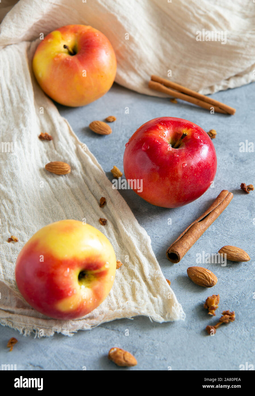 Trois pommes de couleur rouge et jaune avec des bâtons de cannelle, les amandes se situent sur une base de béton gris beige avec un chiffon doux. Orientation verticale. Banque D'Images
