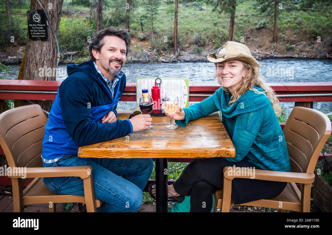 Un homme et une femme assis à une table de patio extérieur le long de la rivière de Chewuch Winthrop, Washington à l'ancienne école Brewery, USA. Banque D'Images