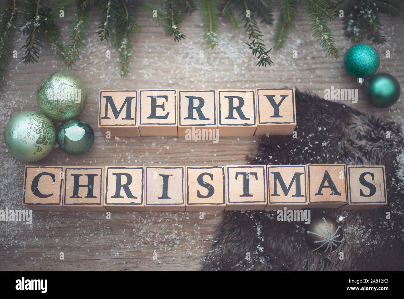 Cubes en bois avec des lettres forme le texte anglais Joyeux Noël. Ils sont couchés sur un fond de bois. Branches de sapin et boules de Noël sont à côté. Banque D'Images