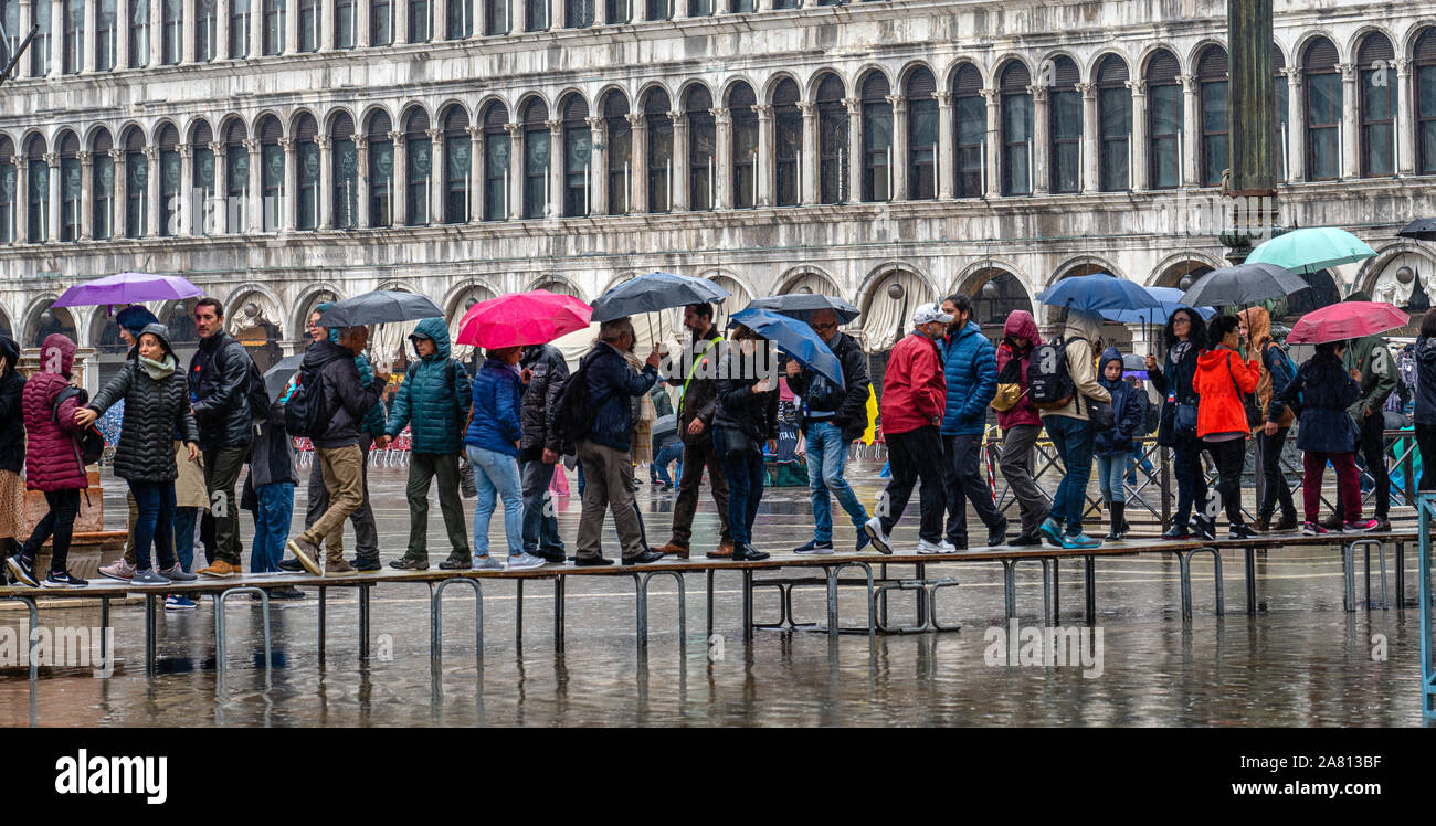 Les touristes à la pluie à l'aide de Venise à marcher à travers un caillebotis a inondé la place St Marc à marée haute Banque D'Images