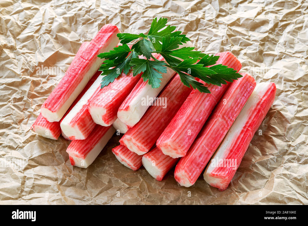 Tas de bâtonnets de crabe surimi de persil sur un papier parchemin froissé. Les fruits de mer et d'ingrédients pour les salades. Une saine alimentation et faire cuire à la maison. Vue de face. Banque D'Images