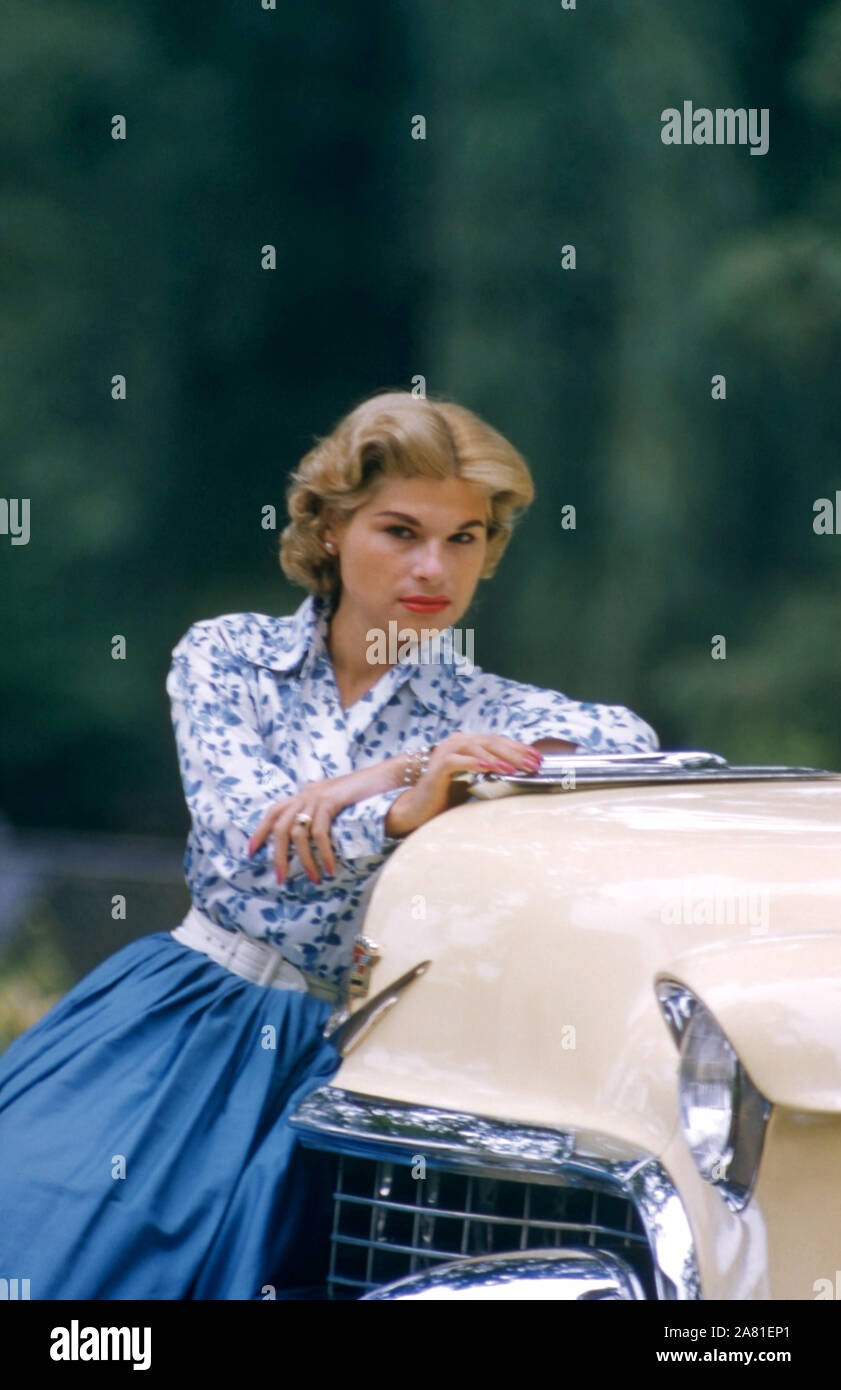 1950 : un modèle non identifié pose dans une robe bleue, assis sur l'extrémité avant d'une voiture vers 1950. (Photo de Hy Peskin) Banque D'Images
