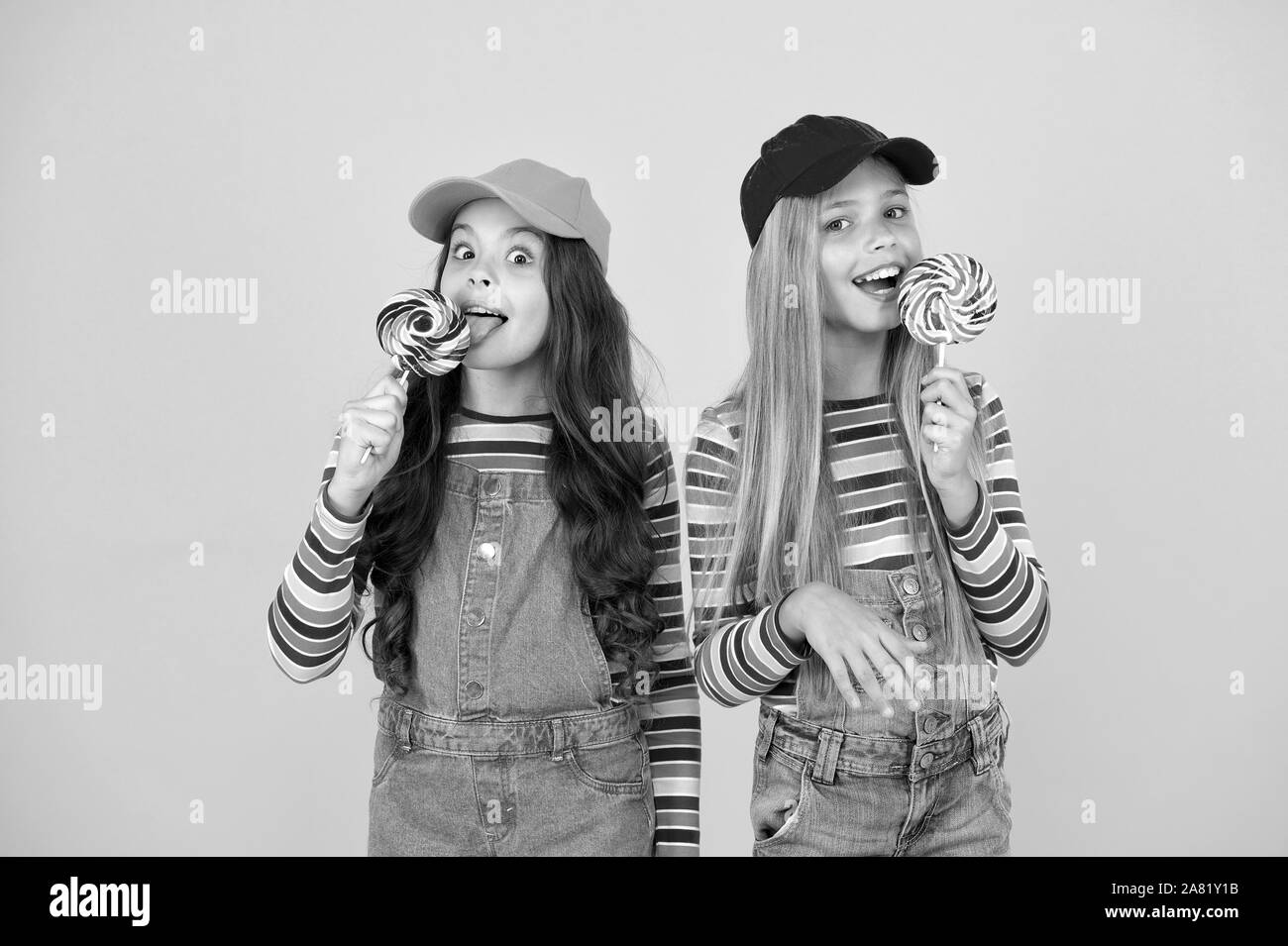 Avoir une couche. Les petites filles bénéficiant délicieux goût de lollipops sur fond jaune. Les petits enfants bonbons à lécher avec goût de fruits classique. Il goûte si bon. Goût sucré de l'enfance. Banque D'Images