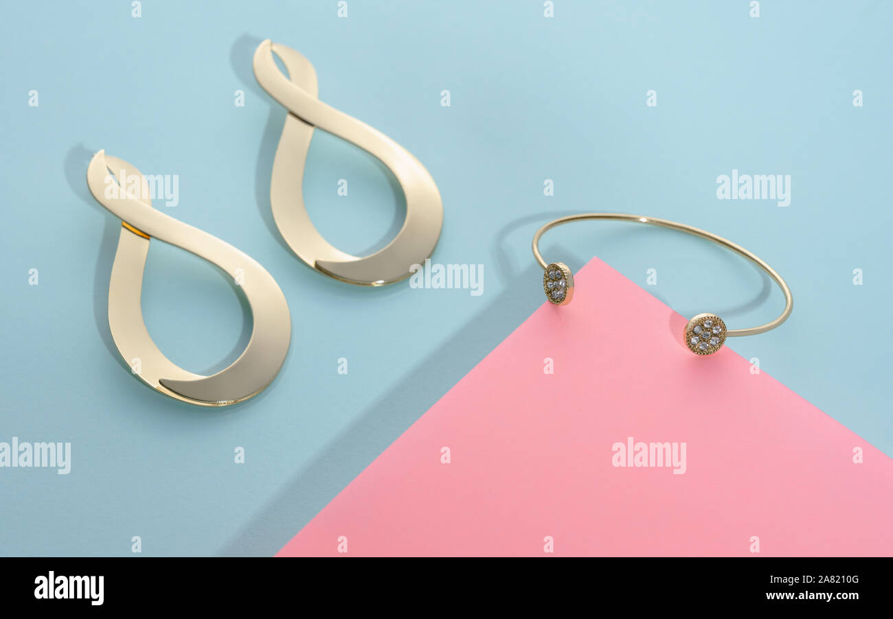 Bracelet en or moderne et l'infini forme anneaux d'or paire sur fond bleu et rose Banque D'Images