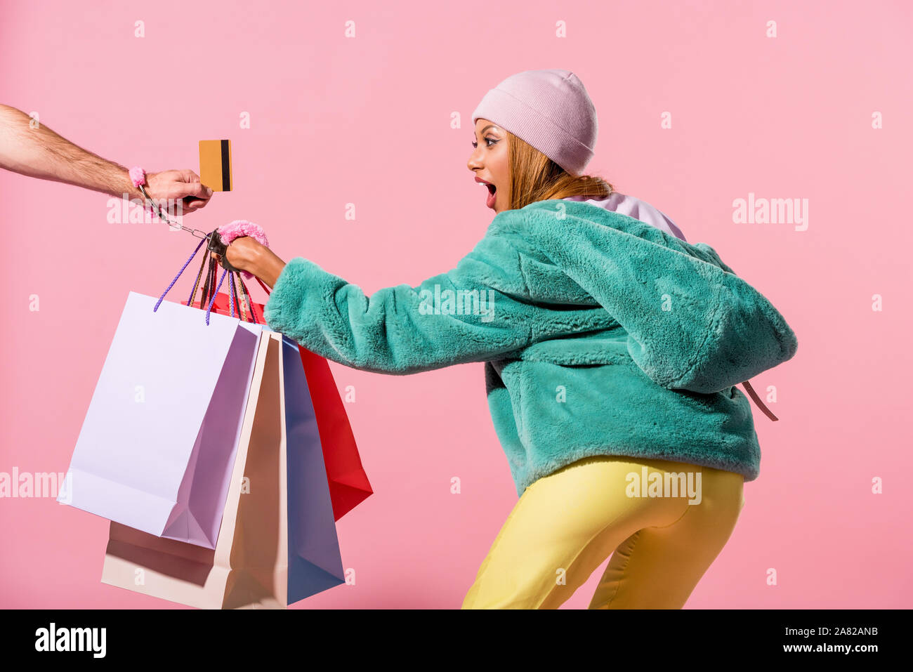 Portrait de l'homme part avec carte de crédit menottés avec des african american woman holding shopping bags sur fond rose, poupée de mode co Banque D'Images