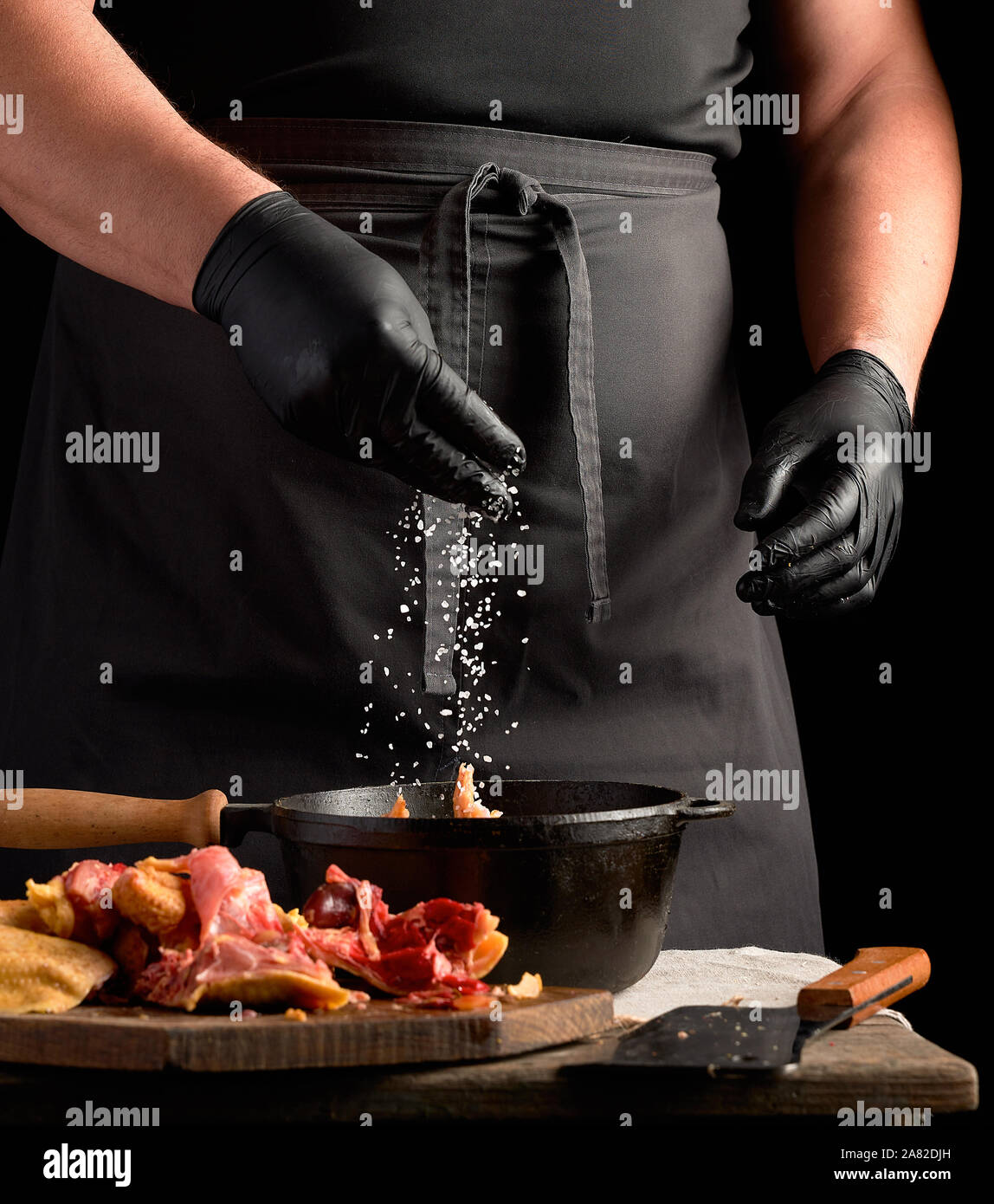 Chef en uniforme noir et des gants en latex saupoudre avec sel blanc de  poulet cru dans une poêle en fonte, la cuisine Photo Stock - Alamy