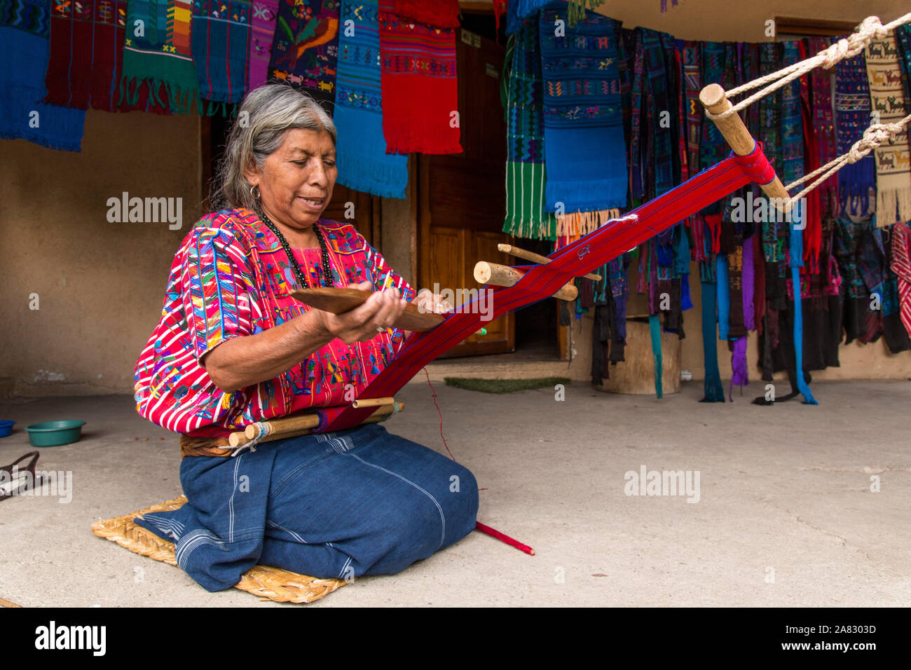 Un vieux aux cheveux gris, femme maya tisse le tissu sur un métier à l'aide tandis que à genoux sur le sol de sa maison à Santa Catarina Palopo, Guatemala. Banque D'Images