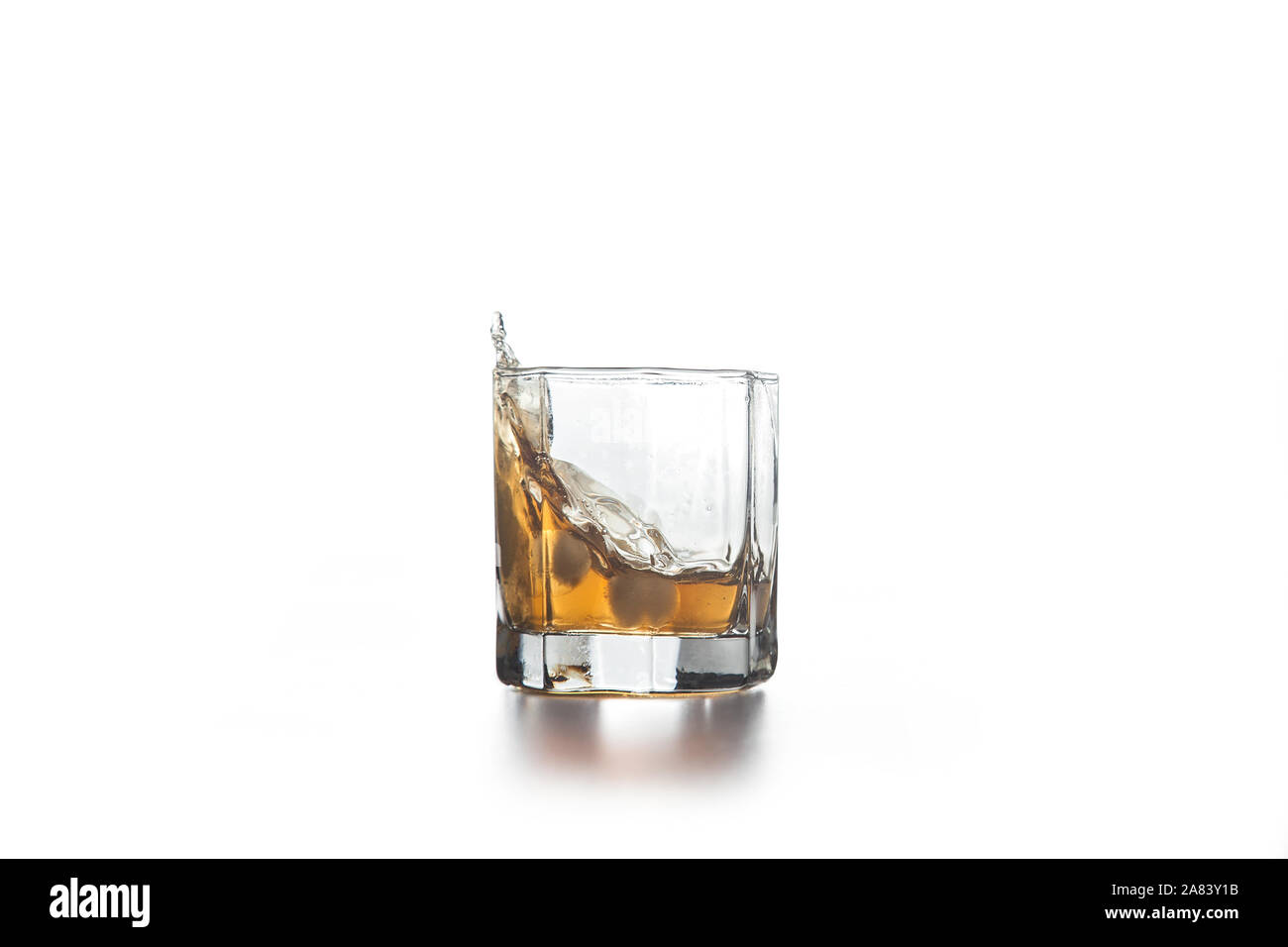 Splash de whisky en verre, de nombreuses gouttes de boissons de verre sur fond clair. Banque D'Images