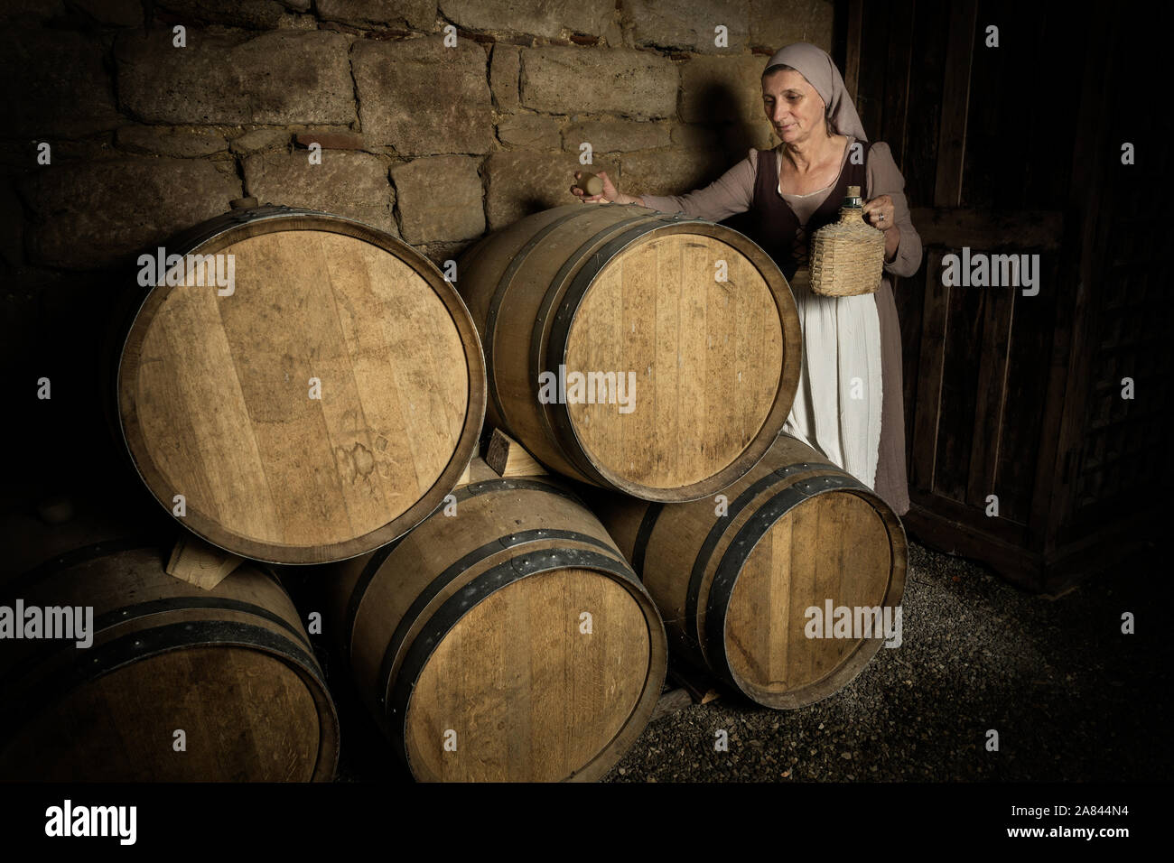 Femme en costume paysan médiéval contrôle de tonneaux de vin dans la cave d'un château médiéval authentique, libéré de la propriété en France Banque D'Images