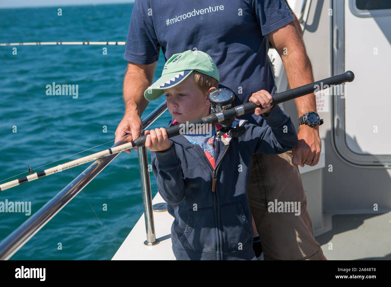 Un jeune garçon tenant une canne de pêche sur un bateau en mer, Devon, Royaume-Uni. Banque D'Images