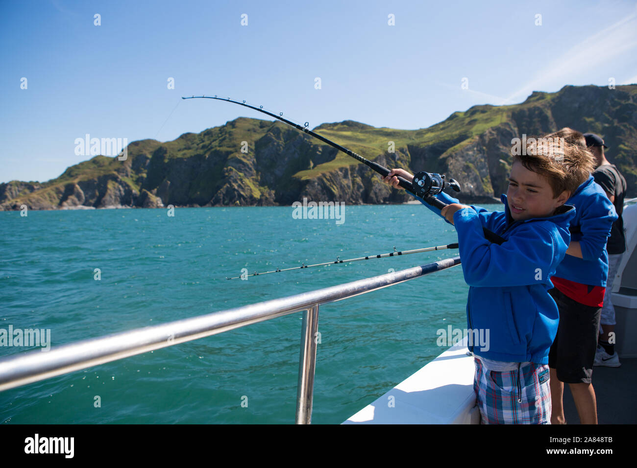 Un jeune garçon tenant une canne de pêche sur un bateau en mer, Devon, Royaume-Uni. Banque D'Images
