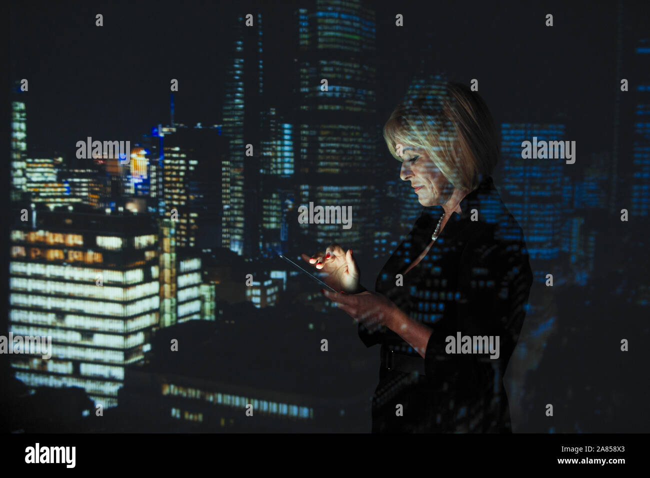 Double exposition businesswoman using digital tablet contre highrise des lumières dans la nuit Banque D'Images