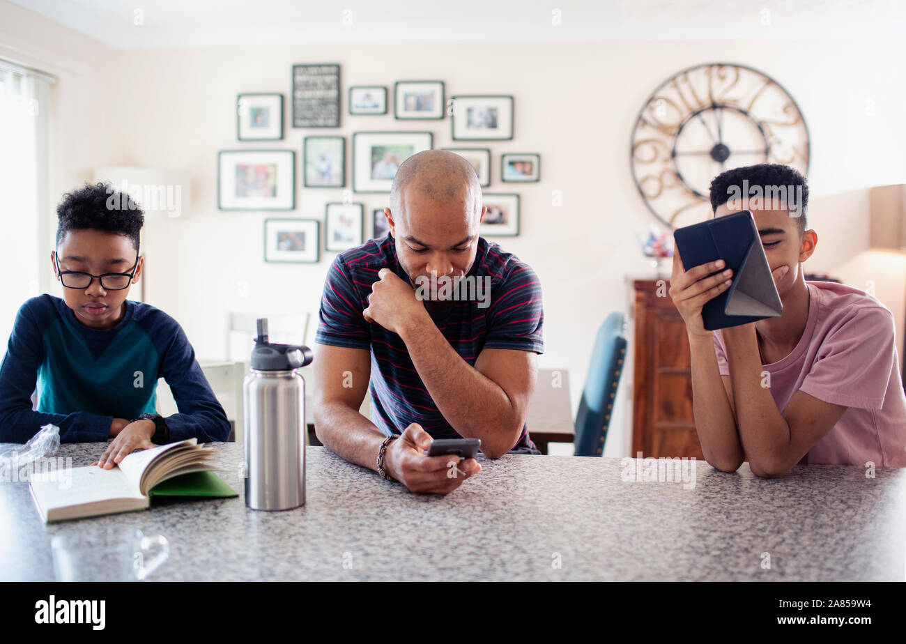 Père et fils, smart phone and reading book in kitchen Banque D'Images