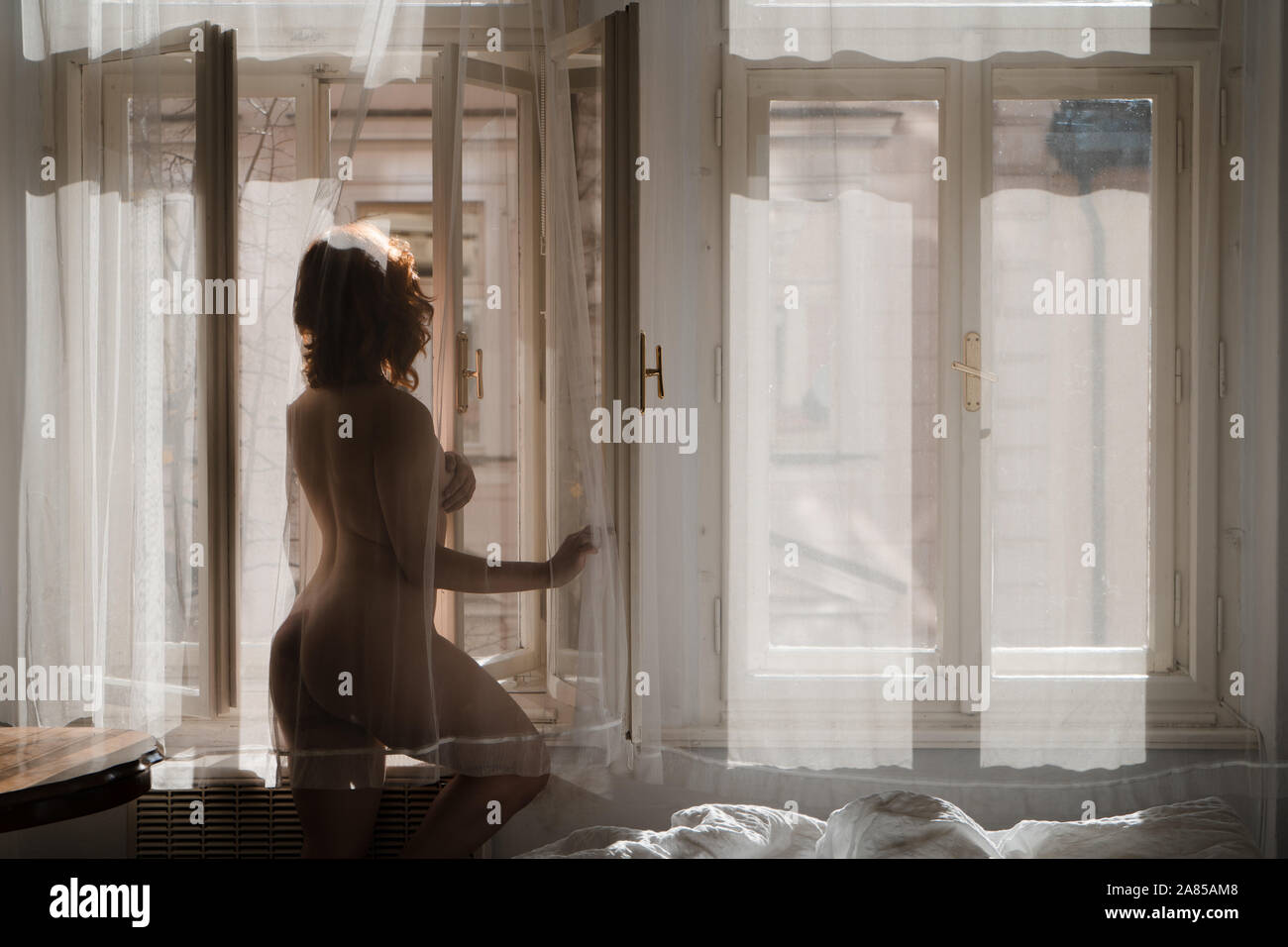 La femme rousse grasse matinée ensoleillée dans une chambre vintage avec pas de vêtements et parties du corps nu - se cacher derrière les rideaux Banque D'Images