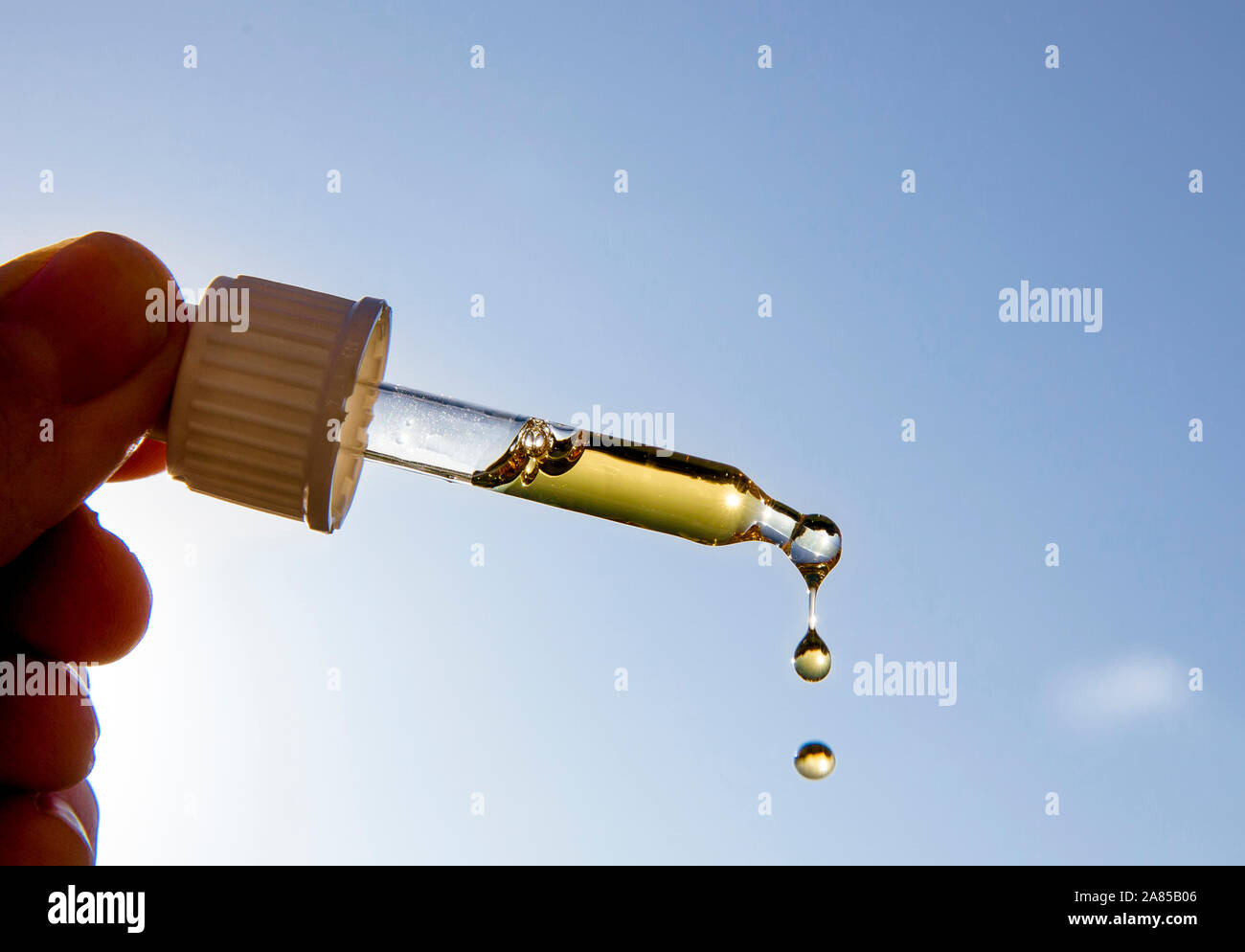 Hand holding pipette compte-gouttes avec de belles liquide d'or-vitamine contre soleil et ciel bleu sur la journée ensoleillée. La vitamine D vous permet de rester en santé pendant l'absence de soleil dans Banque D'Images