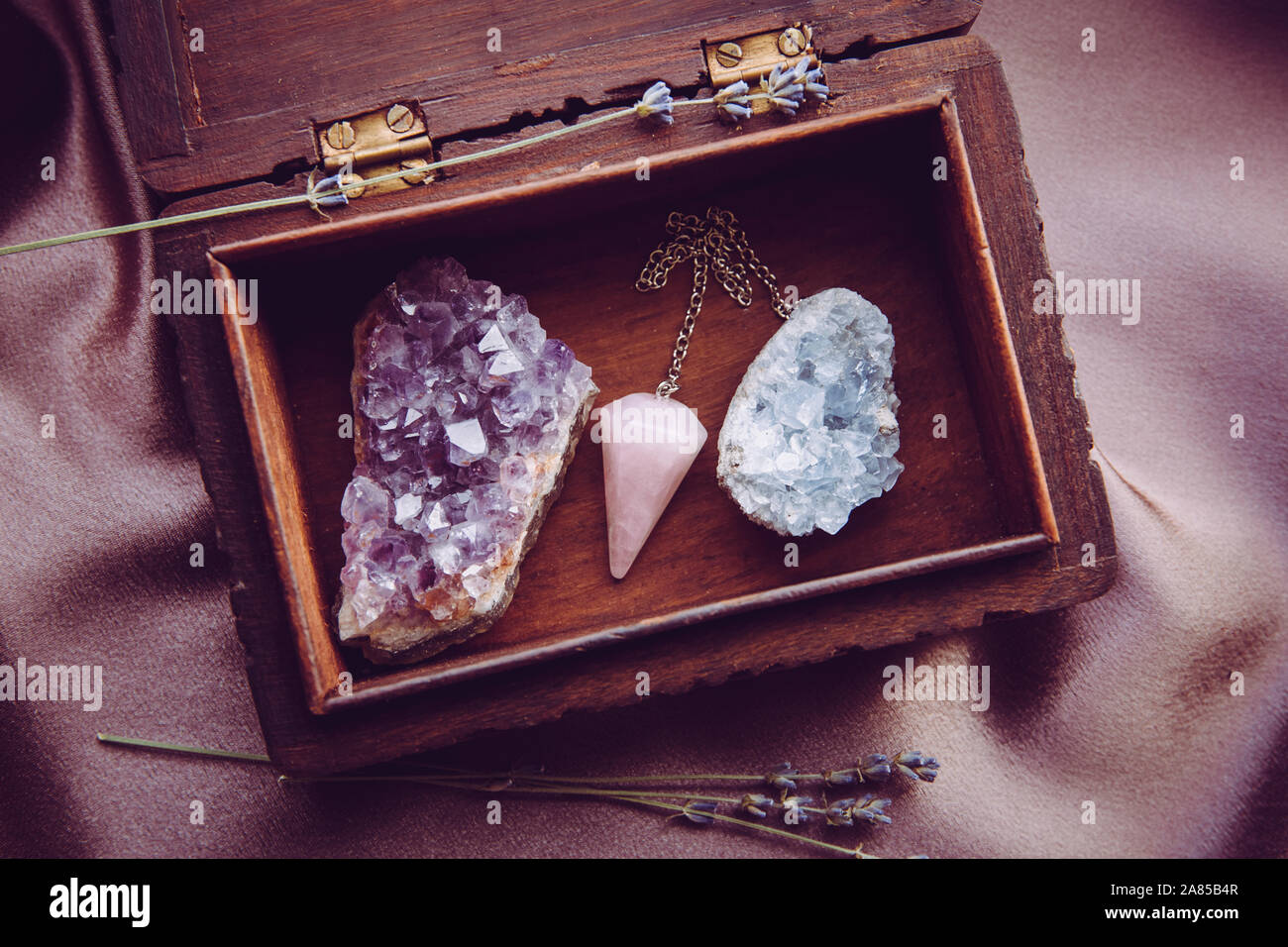 Sorcière outils à l'intérieur belle ancienne boîte en bois. Pendule à quartz rose, amas de cristaux d'améthyste naturel et de célestite. Fleurs de lavande sèches sur violet foncé Banque D'Images