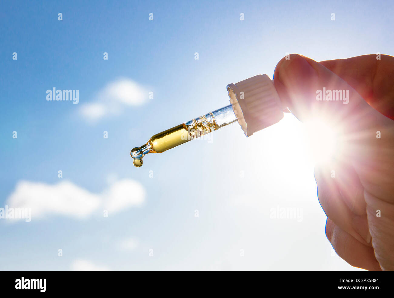 Hand holding pipette compte-gouttes avec de belles liquide d'or-vitamine contre soleil et ciel bleu sur la journée ensoleillée. La vitamine D vous permet de rester en santé pendant l'absence de soleil dans Banque D'Images