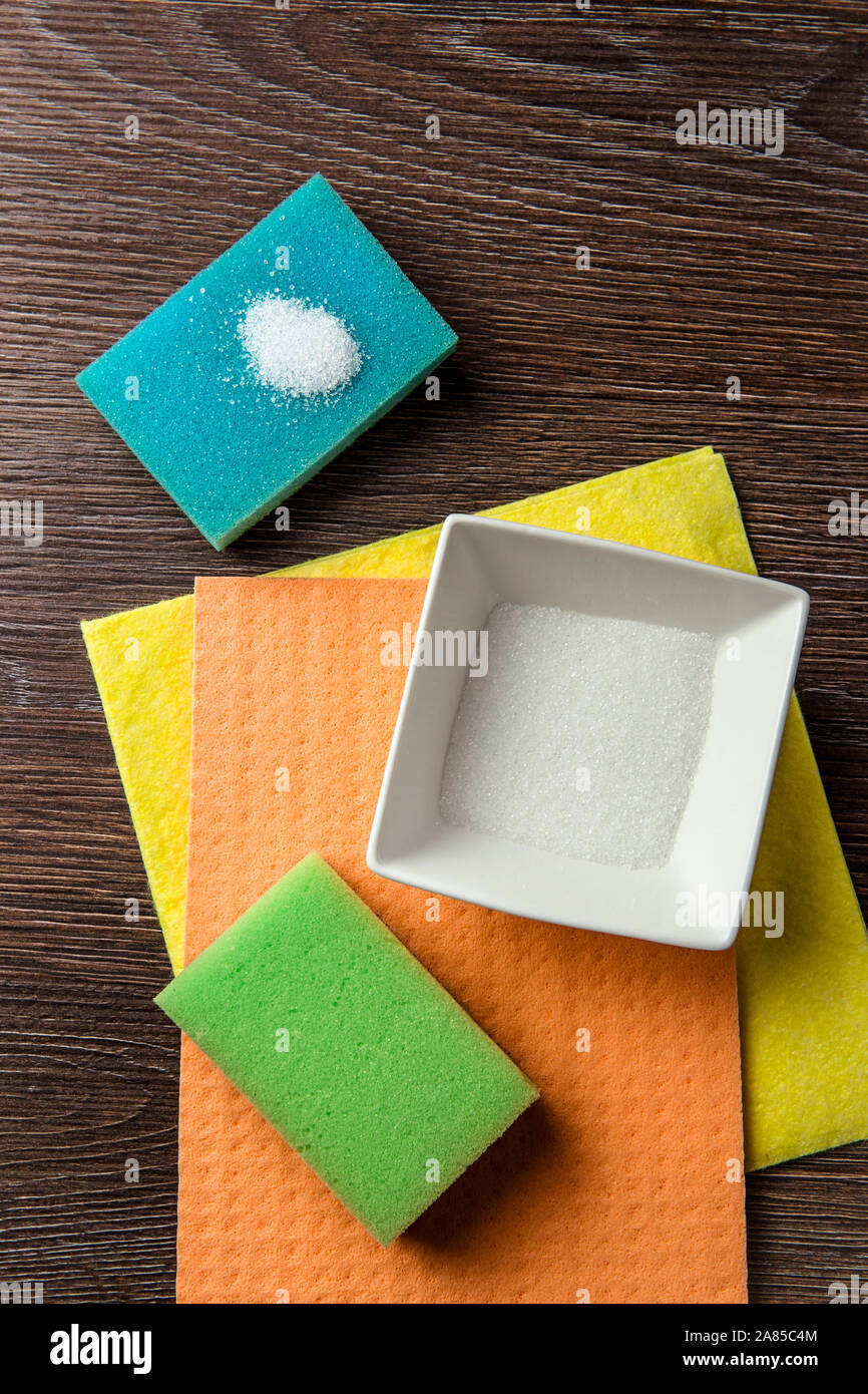 L'acide citrique organique naturelle produits de nettoyage concept. L'acide citrique en poudre blanc carré blanc bol et sur bleu, vert, orange et lave-éponge. Banque D'Images