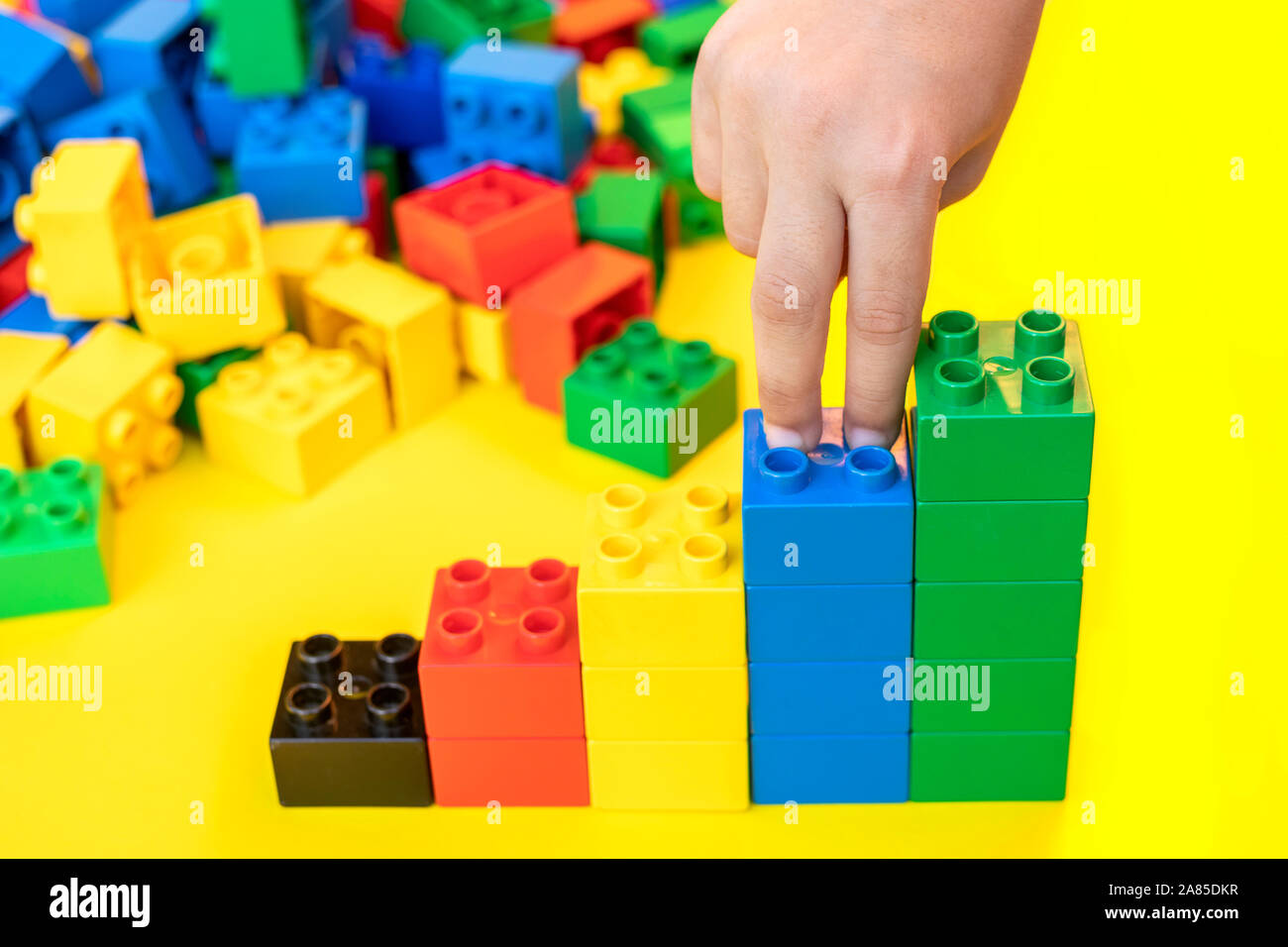 Les doigts à monter sur les graphiques à barres piles jouets blocs de construction en plastique briques sur fond jaune. Banque D'Images