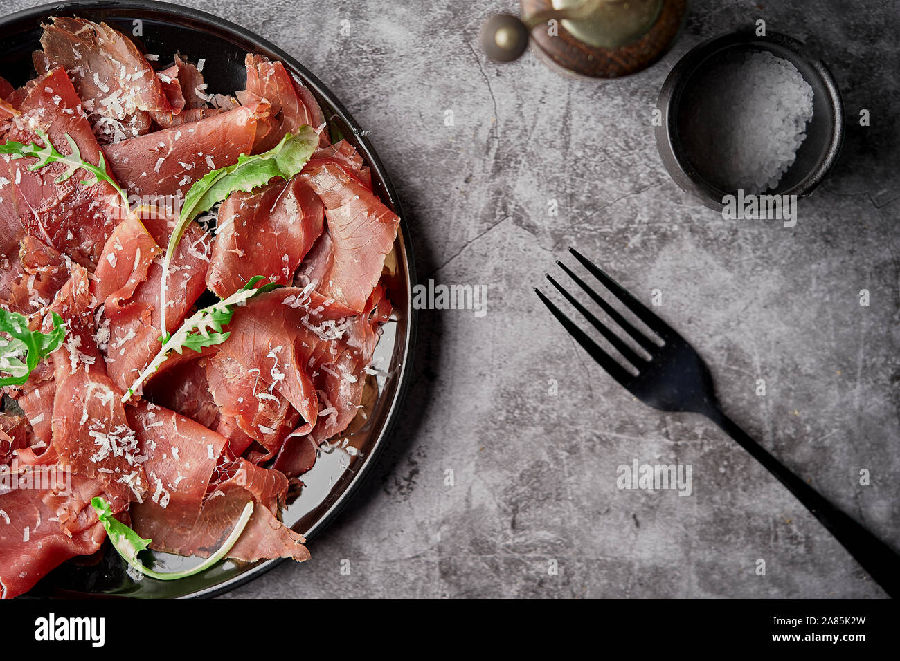 Appétissant savoureuse cuisine italienne classique bresaola avec salade de roquette et parmesan sur fond noir ardesia. Voir formulaire ci-dessus. Vue d'en haut. L'horizontale Banque D'Images