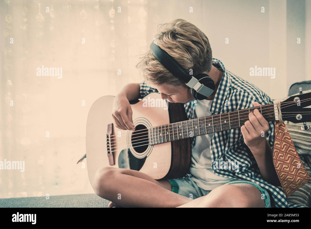 Beau jeune garçon jouant de la guitare acoustique avec le casque. Exercices  de l'élève la musique seule à la maison. Trendy caucasien enfant joue de  divers instruments assis o Photo Stock -