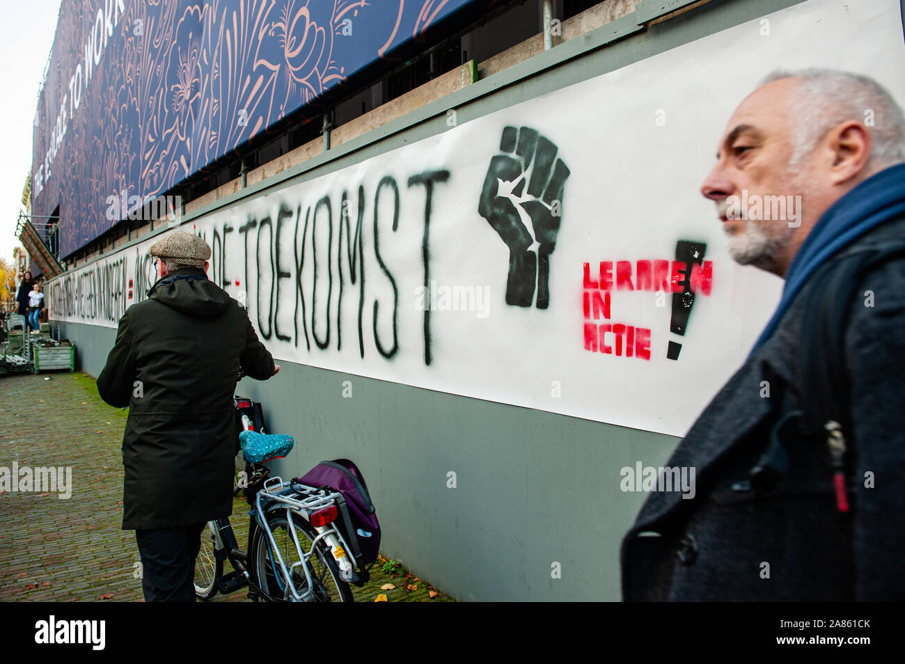 La Haye, Pays-Bas. 06 Nov, 2019. Un homme passe par une grande bannière de la manifestation.Une grève des enseignants nationaux sont allés de l'avant après des syndicats a déclaré que leurs demandes de financement supplémentaire pour le secteur n'avait pas été respecté. Des milliers d'enseignants se sont rassemblés dans plusieurs villes du pays pour exiger l'écart salarial entre les écoles primaires et secondaires à être fermé, et leur charge de travail d'être réduit. La Chambre des Représentants (de Tweede Kamer) va discuter le budget de l'éducation ce même jour. À La Haye, plusieurs événements ont eu lieu. Credit : SOPA/Alamy Images Limited Live News Banque D'Images