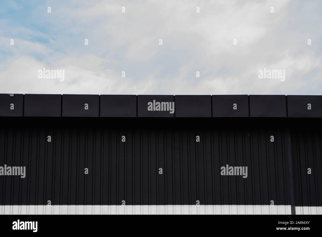 Noir et blanc surface texture feuille de métal ondulé sur la paroi d'un immeuble avec un ciel nuageux. Fond en acier galvaniser. Banque D'Images