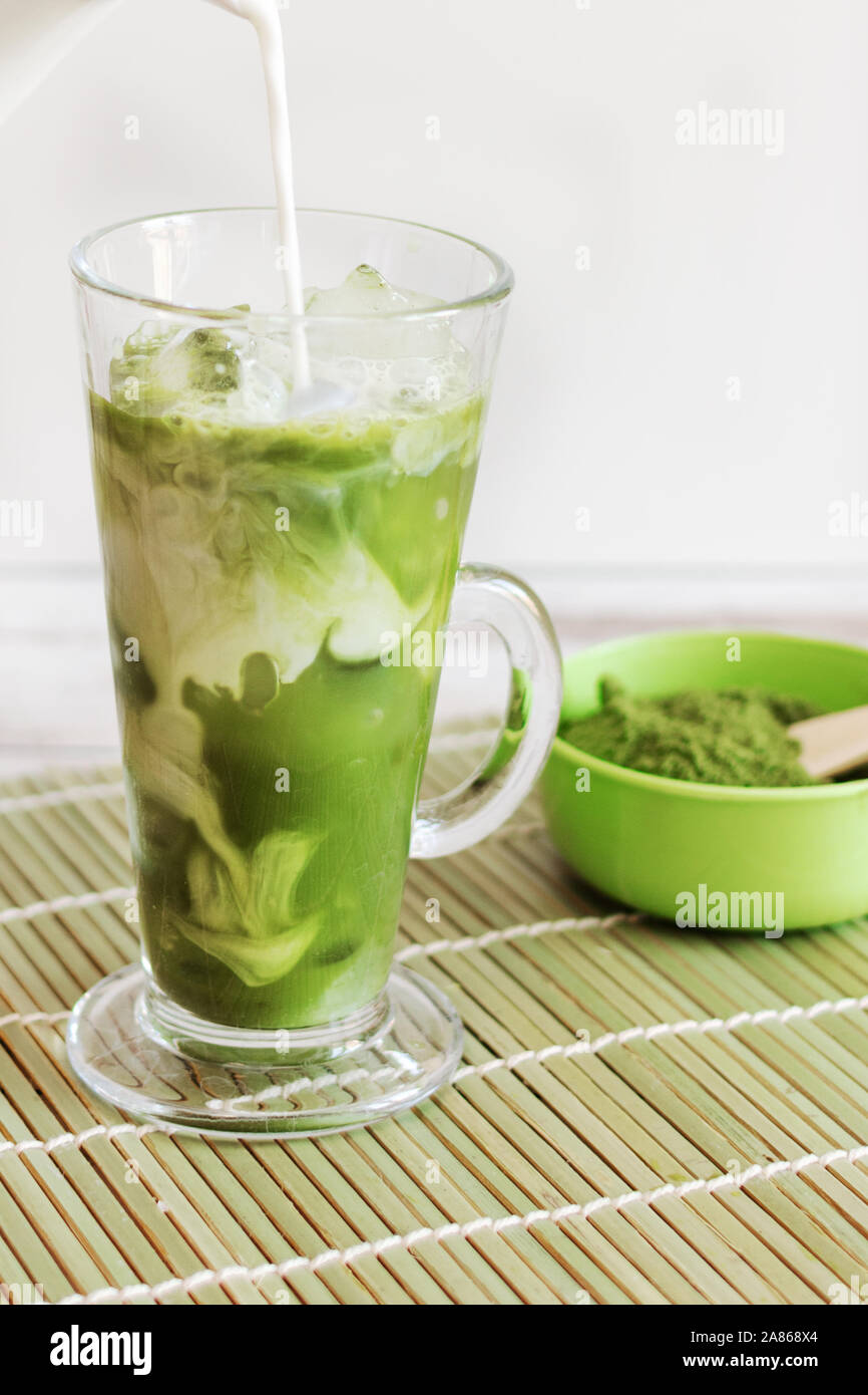 Matcha latte glacé dans un verre Tumbler glass avec le lait de coco verser de pitcher à la main, exemplaire de l'espace. Boissons rafraîchissantes d'été vegan boisson froide. Banque D'Images