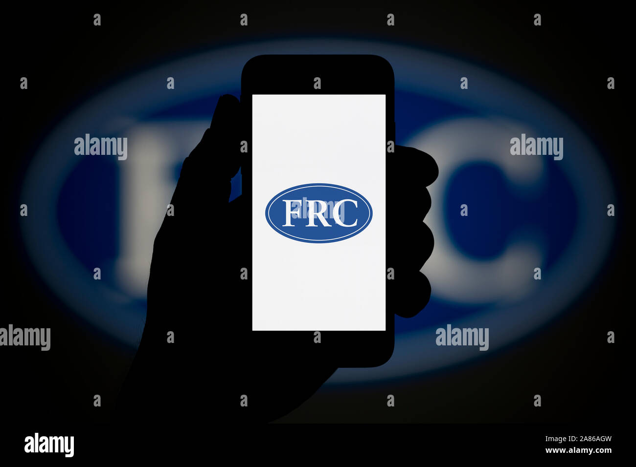 Un homme se penche sur son iPhone qui affiche le Financial Reporting Council (FRC) logo, avec le même logo en arrière-plan (usage éditorial uniquement). Banque D'Images