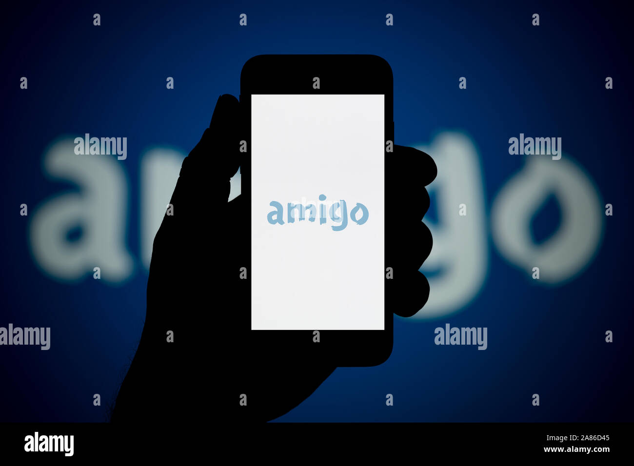 Un homme se penche sur son iPhone qui affiche le logo prêts Amigo, avec le même logo en arrière-plan (usage éditorial uniquement). Banque D'Images