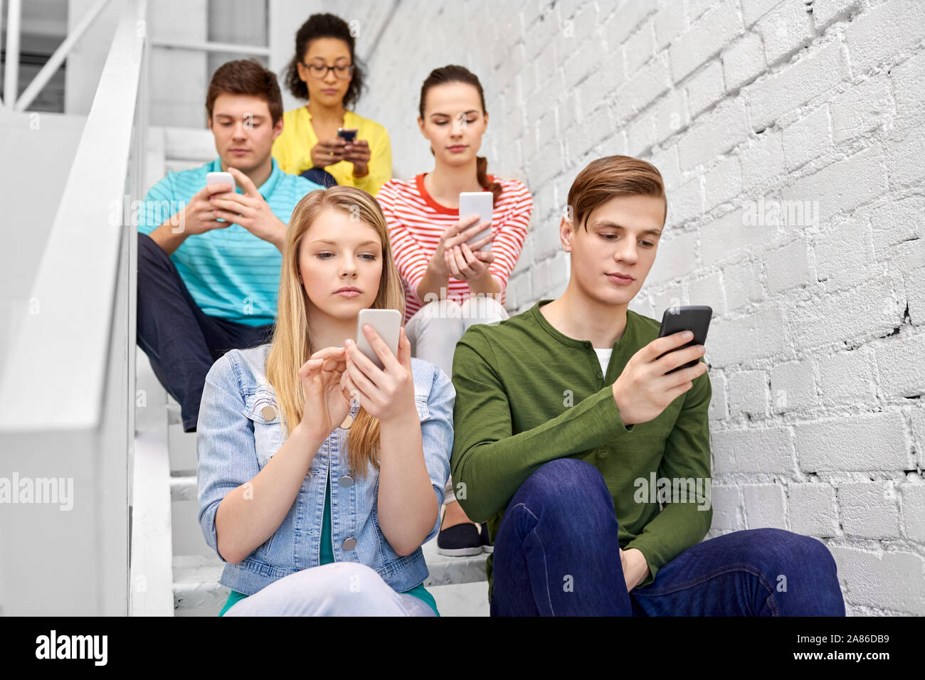 Les élèves assis sur les smartphones avec escaliers Banque D'Images