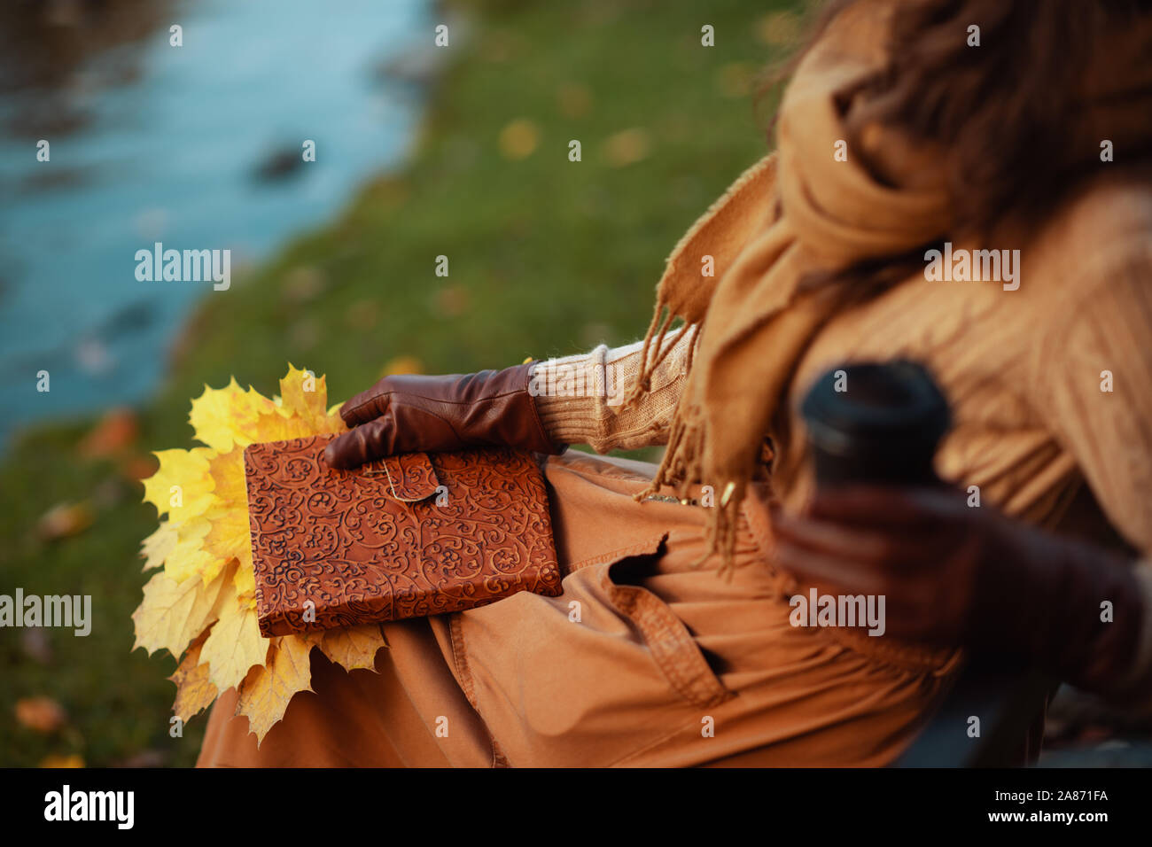 Bonjour l'automne. Gros plan sur l'âge moyen élégant femme en pull, jupe, gants et écharpe avec bloc-notes, feuilles jaunes de boire du café tout en étant assis sur un Banque D'Images