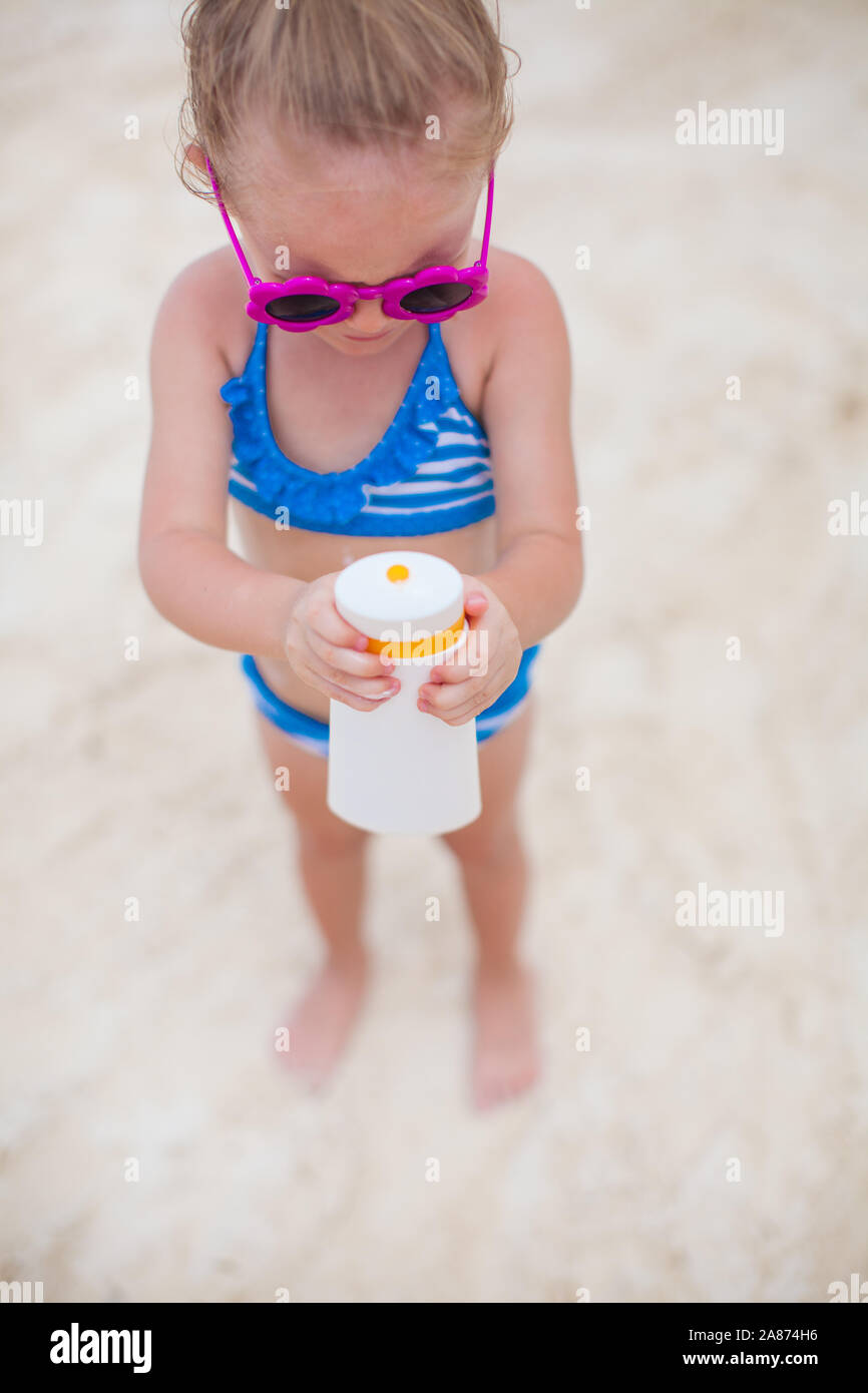 Adorable petite fille en maillot de bain se frotte elle-même d'un écran solaire Banque D'Images