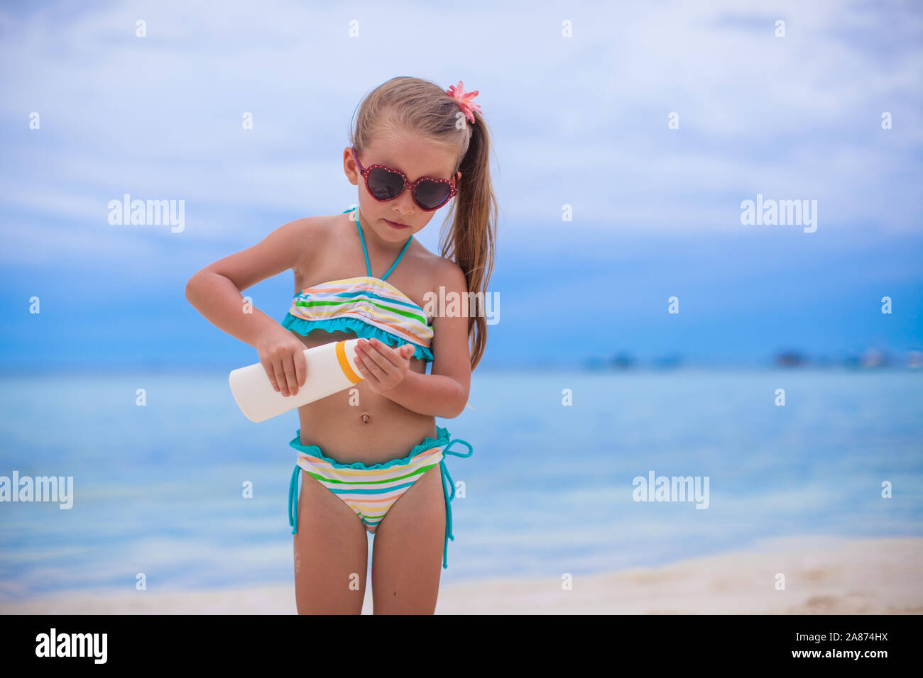 Peu jolie fille en maillot de bain est titulaire d'une lotion solaire bouteille Banque D'Images